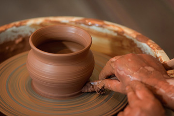 Rotating potter's wheel and clay ware on it taken from above. A sculpts his hands with a clay cup on a potter's wheel. Hands in clay. 