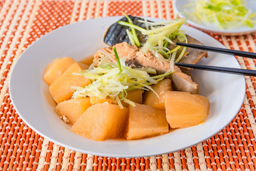 Stew simmered home yellowtail with radish in a plate on a bamboo napkin close up - Japanese and Chinese fish dish