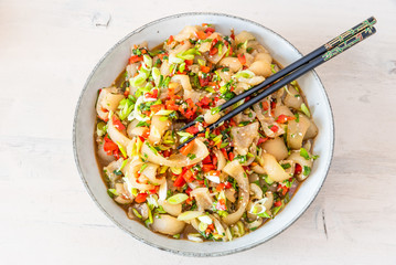 Traditional Asian appetizer - stir-fry spicy sliced pork skin with spices on a plate, close-up, rustic wooden background. Chinese and Thai dish.