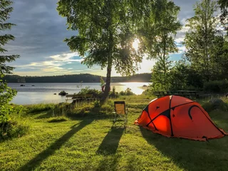 Zelfklevend Fotobehang oranje tent en campingstoel bij een meer, zonsondergang © tronixAS