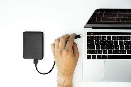 Businessman connected an external hard drive to his laptop on a white table.