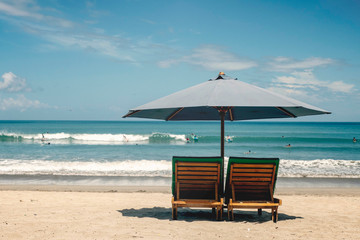 Beach umbrella with deck chairs against the ocean with surfers