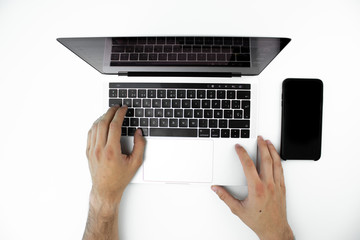 Overhead view of the hands of a person using his laptop on a white table.