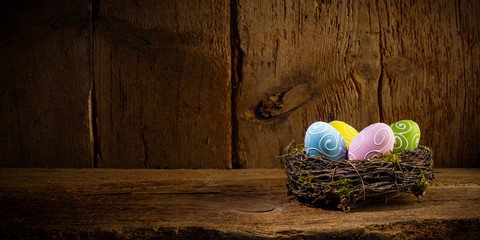 Colorful painted happy easter eggs in birds nest basket on rustic wooden old panorama background...
