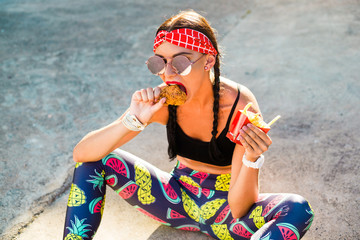 Sports girl in sports clothes, leggings, top, headband, drinks and eats fast food, 80s 90s style