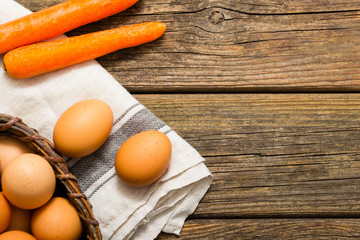 basket of eggs and carrots, old weathered wooden background
