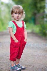 cute two years old blonde white girl in red pants full-size standing on summer outdoor background