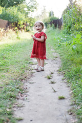 cute two years old blonde white girl in red dress full-size standing on summer outdoor background