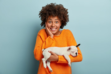 Joyful dark skinned woman laughs sincerely, has broad smile, carries little tired asleep white...