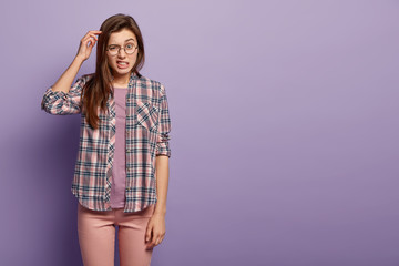 Horizontal shot of confused European young woman scratches head, has indecisive expression,...