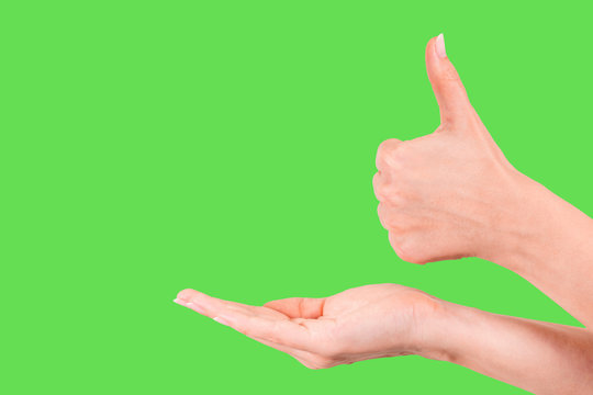 Young girl with beautiful pink manicure holding hand as if showing something virtual and invisible on palm. Other female hand in gesture with thumb up. Close up of hands isolated on green background.
