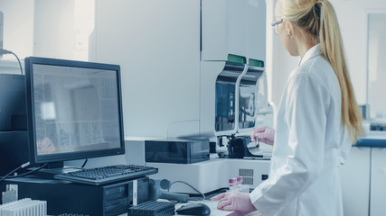 Female Research Scientist Working with Medical Analyzing Machine for Testing Tubes with Blood...