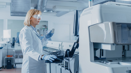 Naklejka premium In Laboratory Female Scientist Analyzes Test Tube Data with Blood Samples with Personal Computer. Team of Researchers Work in Pharmaceutical Laboratory.
