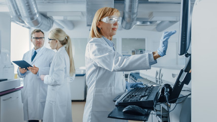 Male and Female Scientists Talking, Using Digital Tablet, Senior Ressearchers Programs Analyzing Equipment. People Working on Genetics Research Project in Innovative Laboratory.