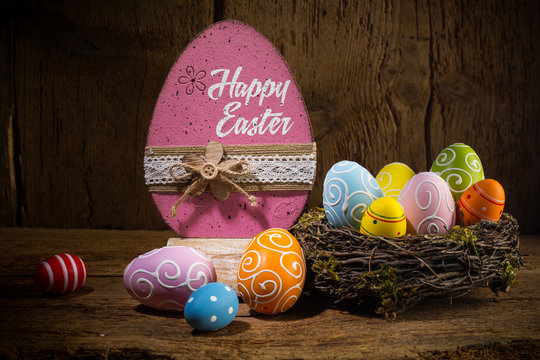 Colorful painted happy easter greeting card eggs in birds nest basket on rustic wooden background - Powered by Adobe