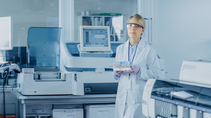 Female Research Scientist Walks Through Laboratory with Tray of Test Tubes Filled with Samples. In the Background People Working in Laboratory with Innovative Equipment.