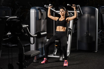 Fototapeta na wymiar Young fit woman flexing muscles on gym machine. Copy space. Sport, fitness, strength training and people concept.