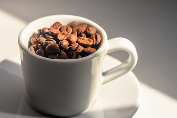 white Cup and saucer with coffee beans poured into it, under the beam of light