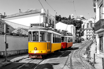 Fototapeta na wymiar Yellow and red vintage trams on old streets of Lisbon, Alfama, Portugal, popular touristic attraction and destination. Black and white picture with a coloured tram.