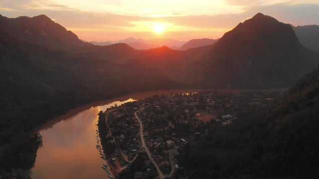 Aerial: flying over Nam Ou River Nong Khiaw Muang Ngoi Laos, sunset dramatic sky, scenic mountain landscape, famous travel destination in South East Asia.