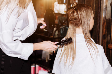 Close-up of hairdresser woman doing hairstyle to client with long blonde hair