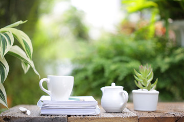 White coffee cup with small plant in white pot on brown wooden table at outdoor