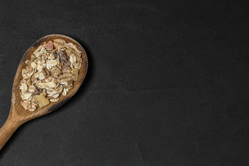 Top view. Wooden spoon with muesli on black plate with copy space
