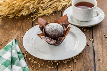 Chocolate muffin in brown paper with cup of tea on wooden table