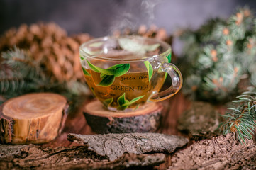 Pot of hot herbal tea, fir cones and paws of blue fir on wooden background
