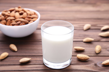 Almond milk in glass with almonds on brown