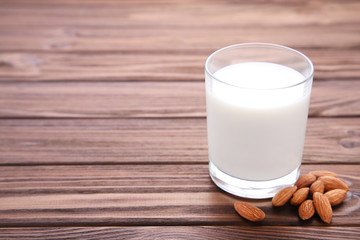 Almond milk in glass with almonds on brown