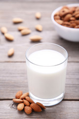 Almond milk in glass with almonds on grey