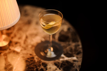 Yellow cocktail in the glass decorated with a lemon zest standing on the marble table