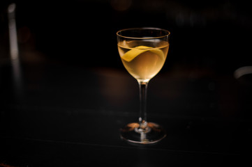 Yellow cocktail in the glass decorated with a lemon zest standing in the dark