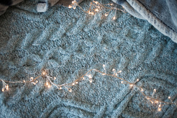 Garland with glowing lights in the background of a fluffy grey blanket