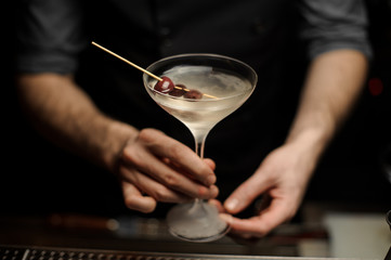 Male bartender serving cocktail decorated with a berries on the skewer
