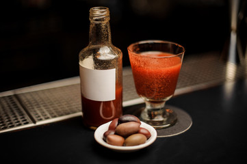 Prepared Bloody Mary cocktail in the bottle and glass decorated with red powder with little plate of olives