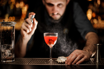 Male bartender spraying on the delicious transparent red cocktail in the glass