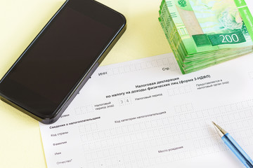 Document in Russian language "of the Tax Declaration on the tax to incomes of physical persons" close-up, pen, smartphone and money for the payment of tax