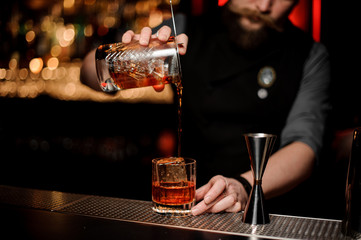 Male bartender pouring a cocktail from the measuring glass cup through the strainer
