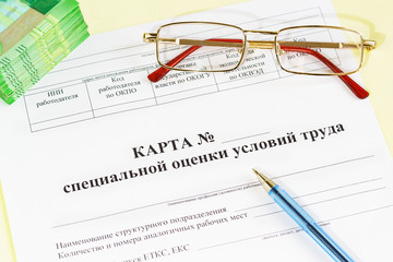 Document in Russian "Map of special assessment of working conditions", glasses, money and a pen on the accounting table