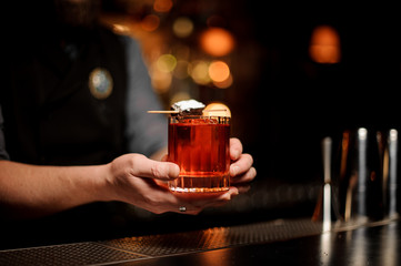 Professional bartender serving a brownie piece on the skewer with a powdered sugar on the cocktail glass
