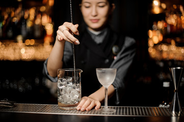 Bartender girl stirring an ice cubes with a steel spoon in the measuring glass cup