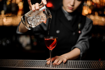 Female bartender pouring an alcohol from the measuring glass cup through the strainer to the cocktail