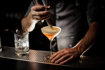 Bartender adding to a cocktail in the glass a whipped cream