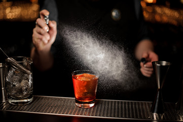 Professional bartender spraying to the cocktail glass with one big ice cube