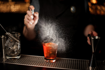 Male bartender spraying to the cocktail glass with one big ice cube