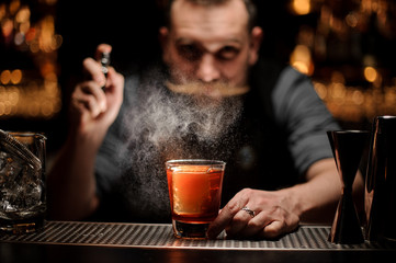 Professional bartender spraying to the cocktail glass with one big ice cube under the light