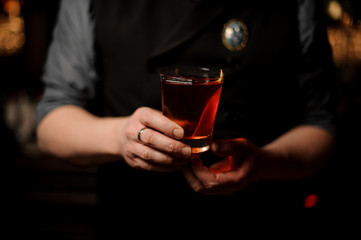Bartender serving a cocktail in the glass with a orange zest as a decor