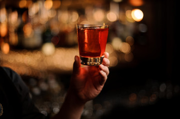 Professional bartender serving a cocktail in the glass with a orange zest as a decor